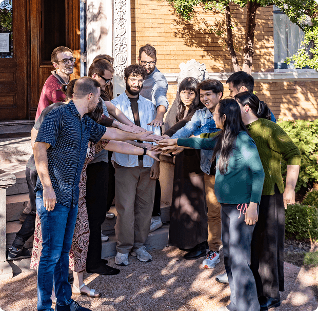Coverbase team members putting hands together in a circle outside a brick building